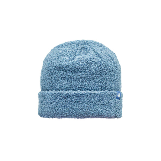 A light blue sherpa beanie featuring a cozy, napped fabric and a small triangular logo patch on the cuff.