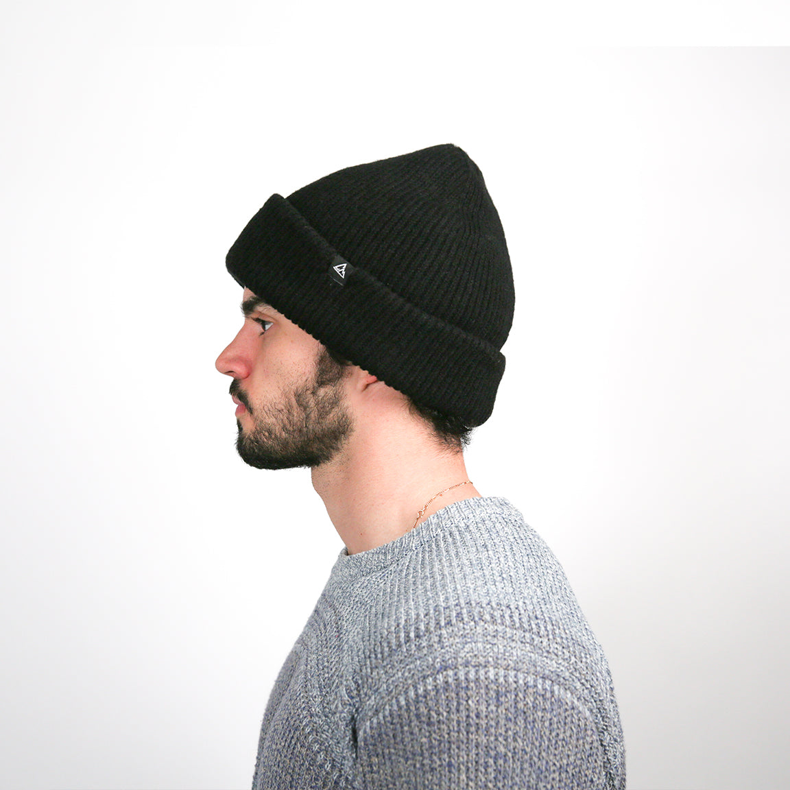 Displayed is a person wearing a classic knit beanie in solid black. The beanie has a ribbed texture with a cuffed brim, providing a snug and comfortable fit for a casual look.