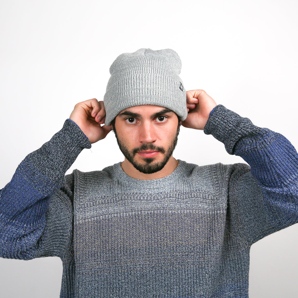 The wearer adjusts the light grey beanie, highlighting its flexible styling and the soft, ribbed texture, which adds a casual touch to the outfit.