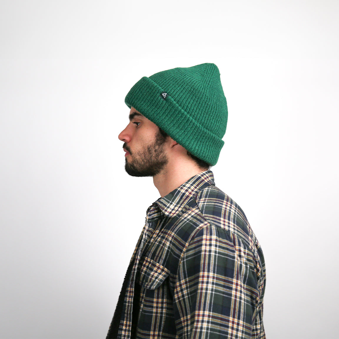 From the side, the forest green beanie's ribbed texture and rolled brim are more apparent, showcasing the hat's snug fit and the richness of its color, suitable for chilly weather.