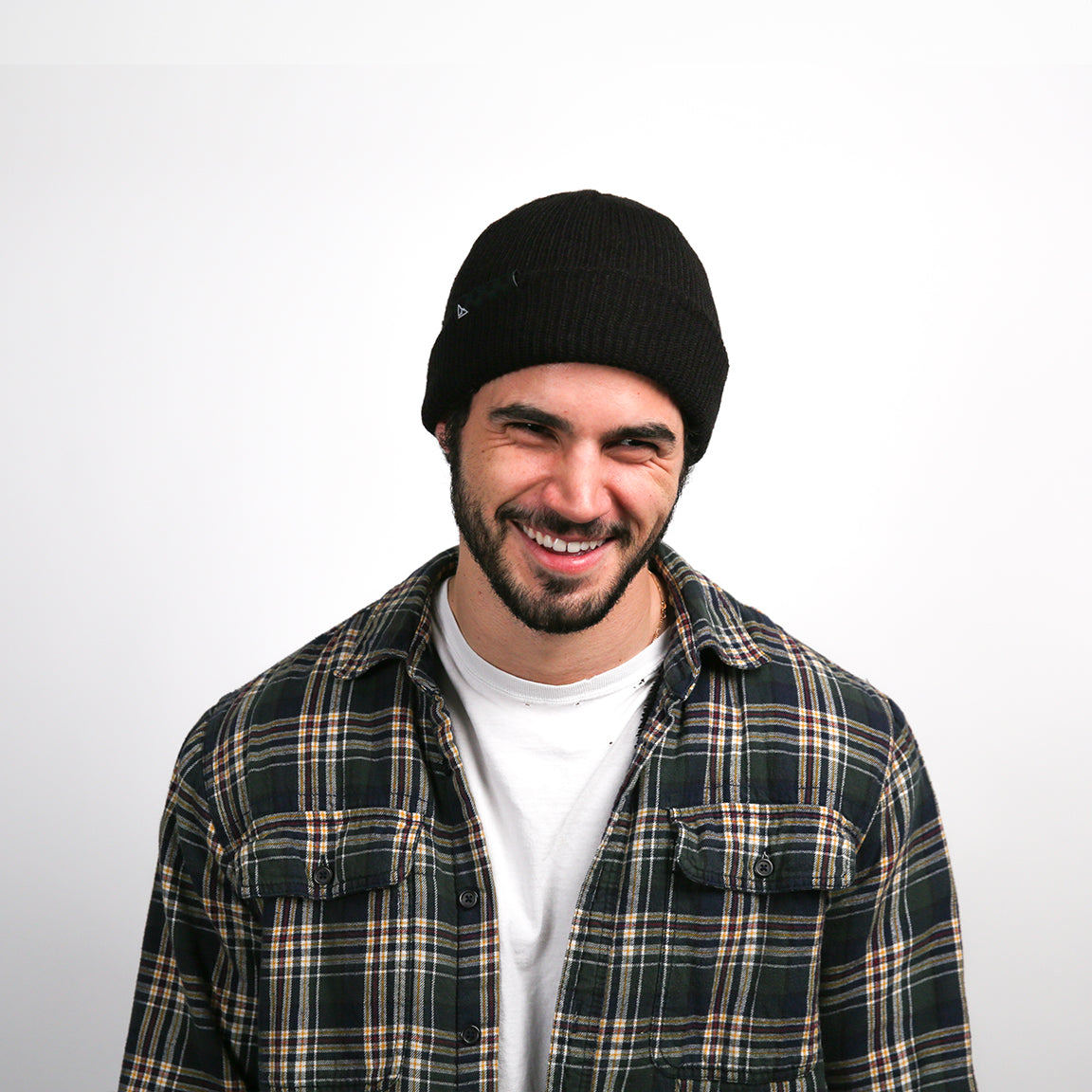 The person in the image is wearing a black ribbed knit beanie with a rolled-up brim. The beanie fits snugly on the head, providing warmth and a touch of style to a casual outfit, highlighted by a genuine smile.