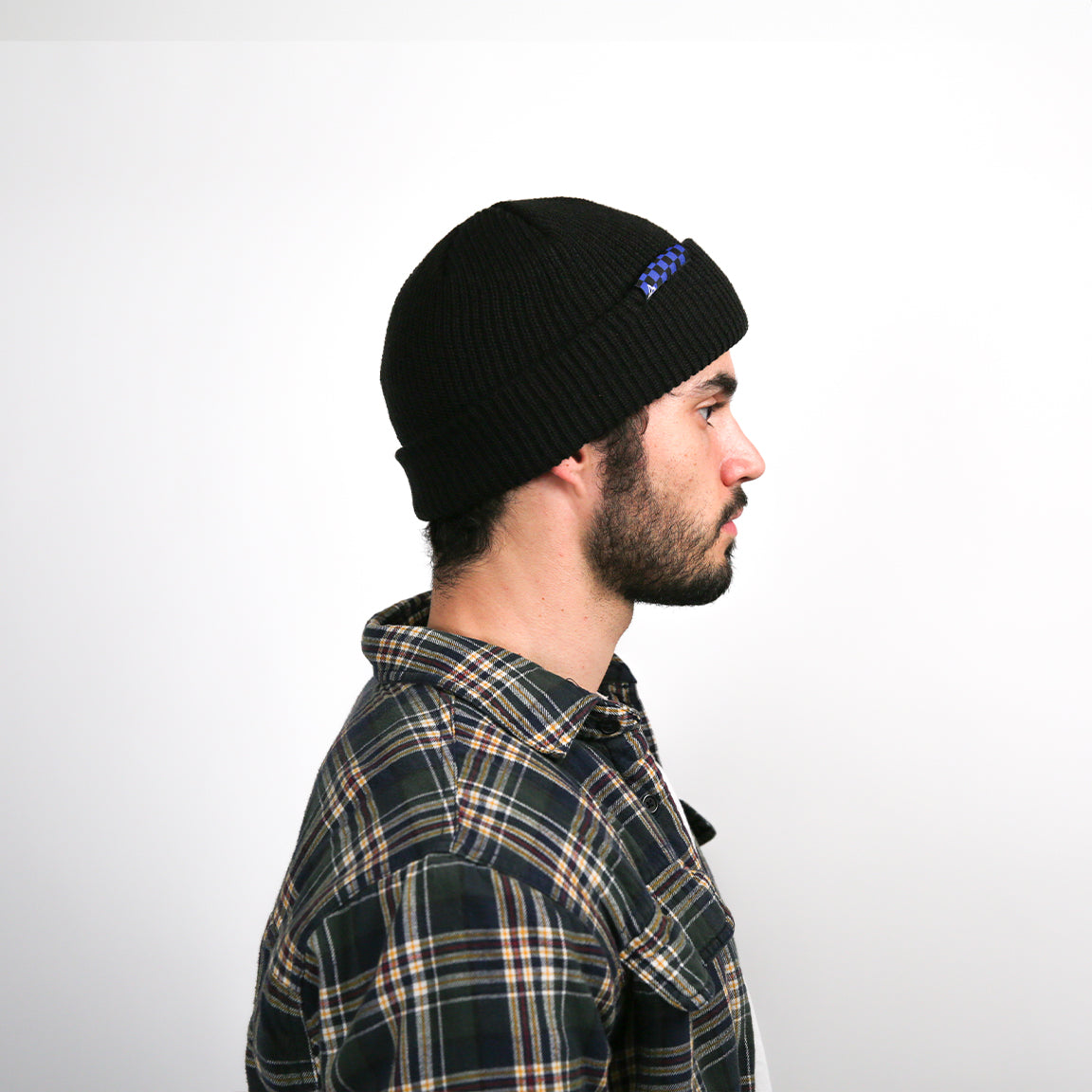 Here, the beanie is shown from the side with a navy and black checkered logo patch, providing a slight variation in design while maintaining the overall look and feel.