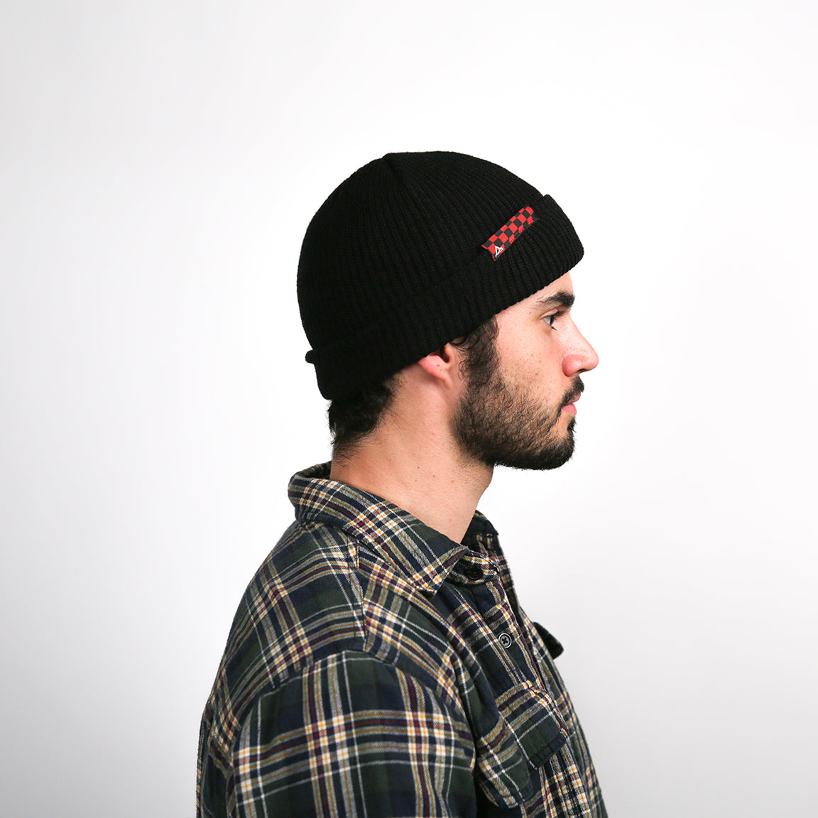 Here, the beanie is shown from the side with a red and black checkered logo patch, providing a slight variation in design while maintaining the overall look and feel.