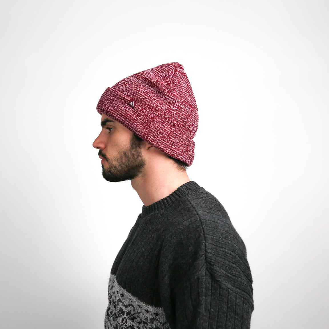From the side, the beanie's heathered burgundy fabric and relaxed fit are evident, along with a small black logo patch that offers a unique detail to the design.