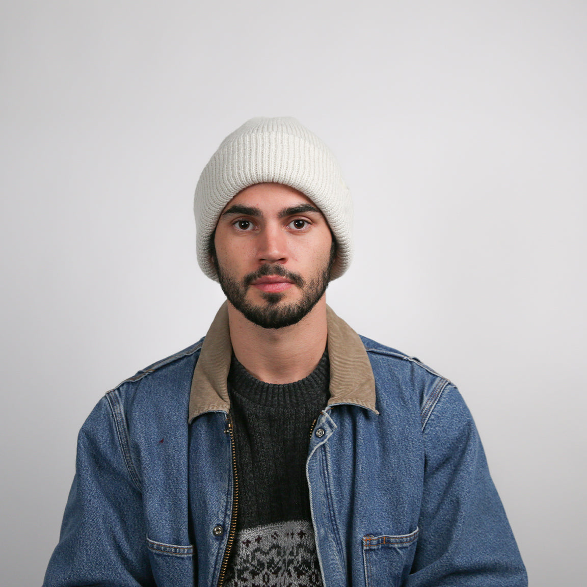 A person is shown wearing a ribbed knit beanie in a crisp white color. The beanie is designed with a cuffed brim, offering a snug fit and a timeless, versatile style.