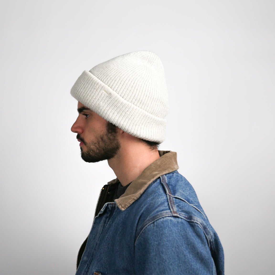 A person is shown wearing a ribbed knit beanie in a crisp white color. The beanie is designed with a cuffed brim, offering a snug fit and a timeless, versatile style.