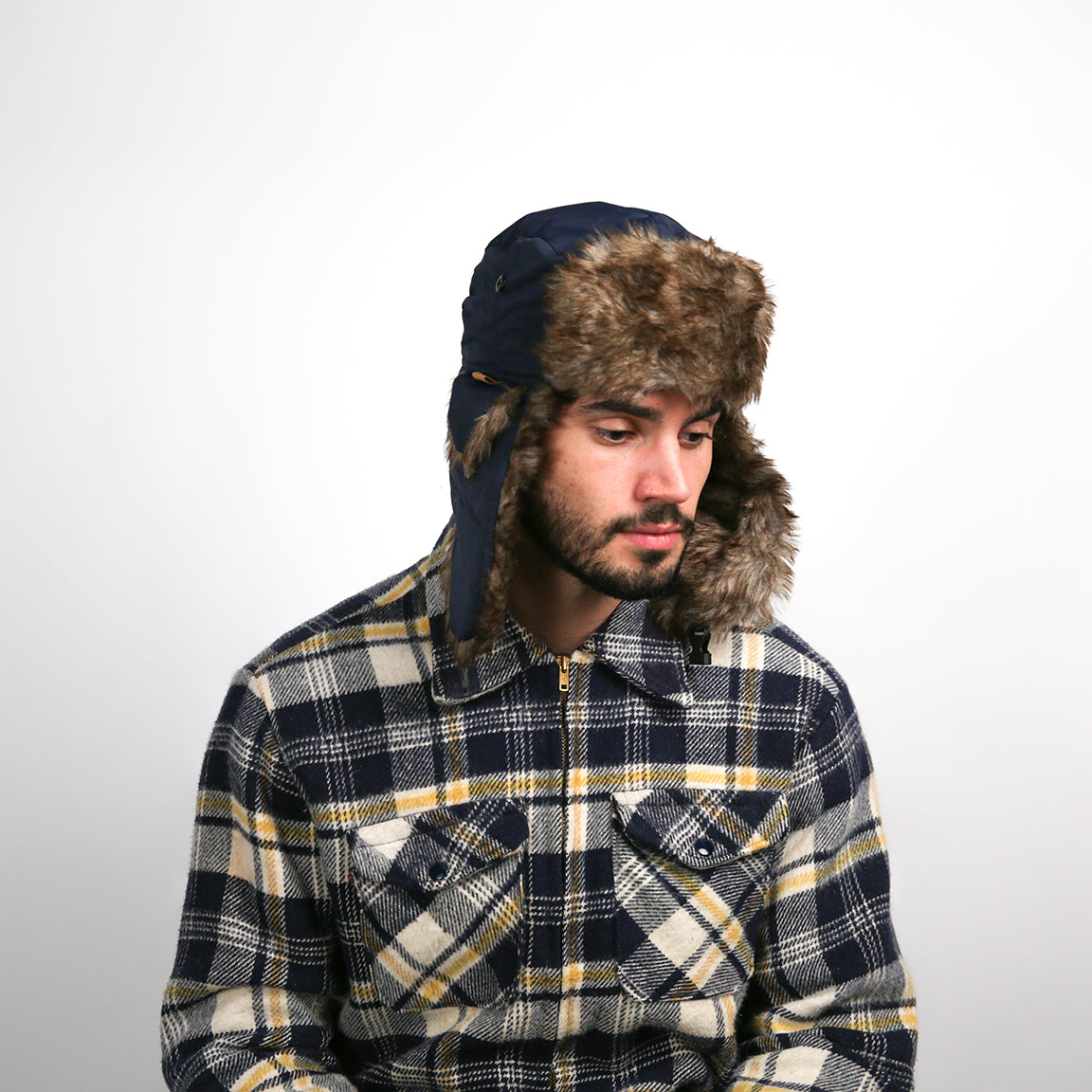 A person is featured wearing a navy blue aviator hat with a brown faux fur lining. The hat includes practical ear flaps and a buttoned chin strap, offering both warmth and style.