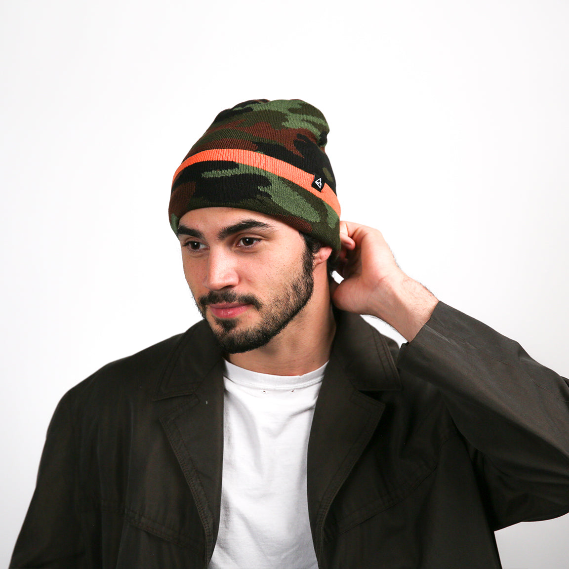 A front-facing view of a beanie with a green, brown, and black camouflage pattern. It features a bright orange stripe and a small black triangular logo near the edge. The beanie is worn loosely, creating a slight slouch at the back.