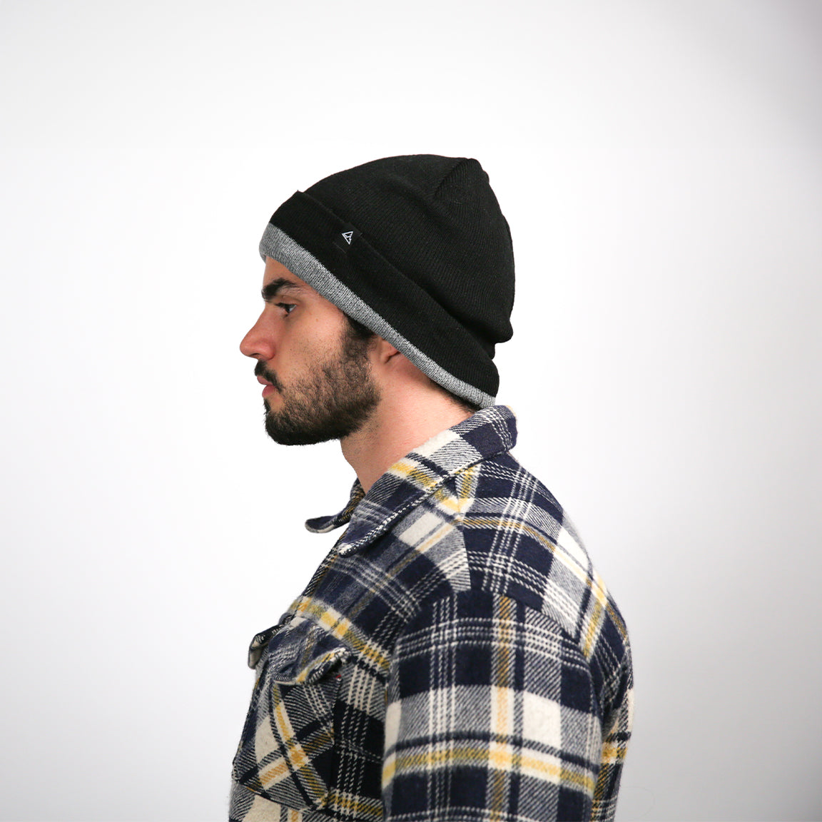 A side profile, the man's beanie, now seen from a different angle, reveals a layered, slouchy style. The same plaid shirt cloaks his upper body, and his facial features are in profile, with the light casting soft shadows on his face, accentuating his jawline and the intensity of his gaze to the side.